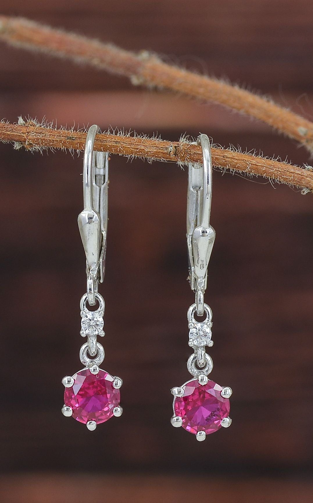 A pair of silver leverback earrings with round pink gemstones and small clear accent stones.